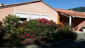 Un edificio de fachada rosa, dos puertas de garaje y un jardín con diversas plantas en flor.
