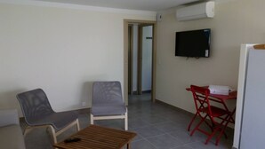 Una habitación con televisión, una mesa, dos sillas y una puerta que da a otra habitación.