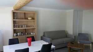 Una sala de estar con un sofá gris, una estantería de madera, una mesa blanca y dos sillas.