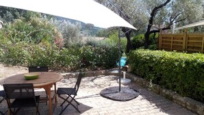 Un patio al aire libre con una mesa redonda, sillas, un paraguas blanco y una silla de metal.