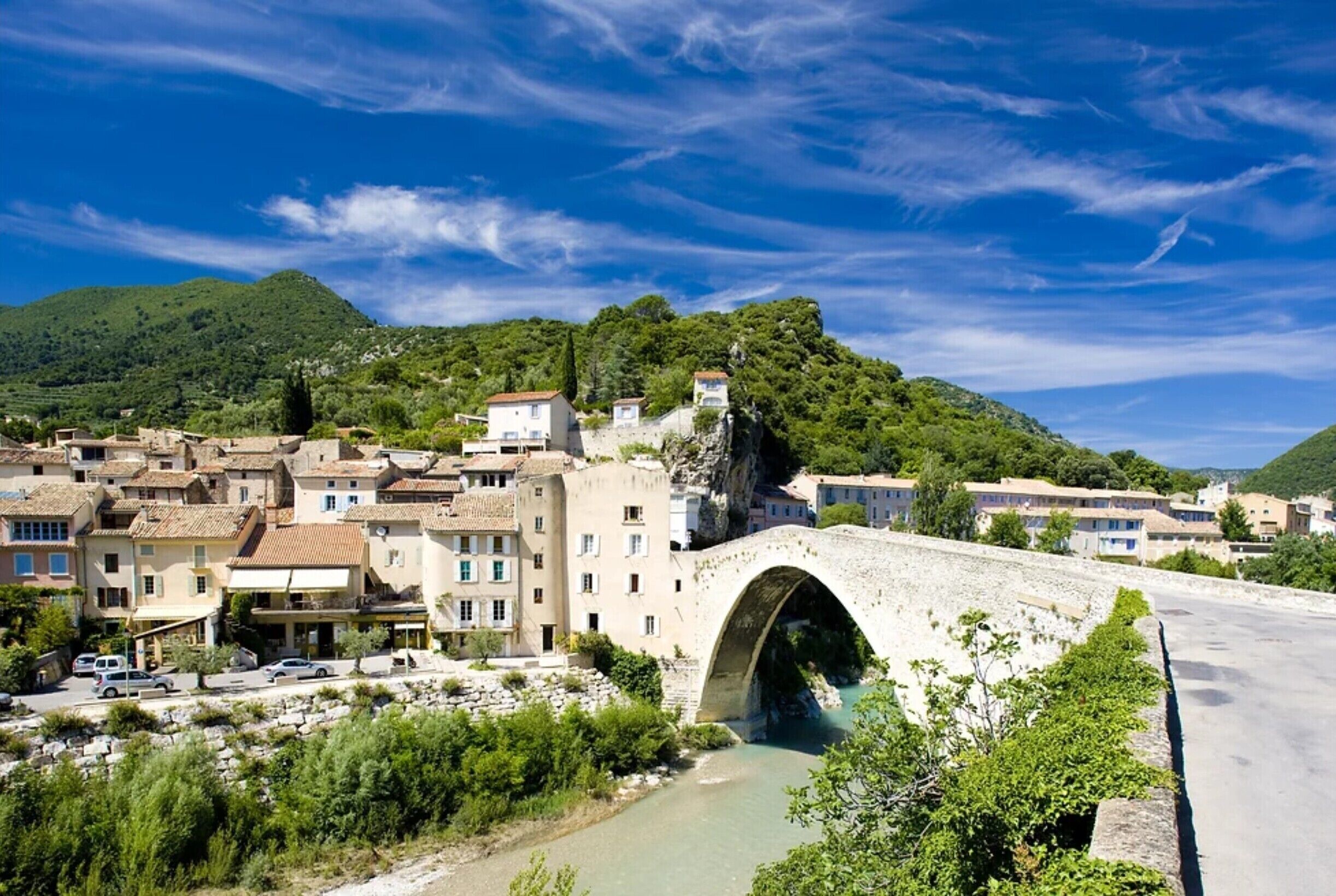 A stone bridge over a river, surrounded by buildings with Mediterranean architecture.