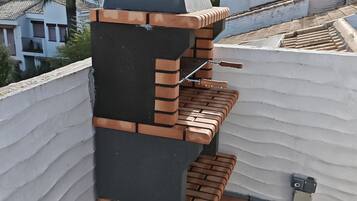 En tagterrasse med grill og skorsten, omgivet af en hvid mur og flisebelagt gulv.