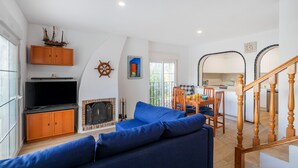 A living room with a sofa, television, fireplace, and a dining area with chairs and a table. - Holiday Home 'Bungalow 213' with Shared Pool, Wi-Fi and Air Conditioning (Santa Pola)