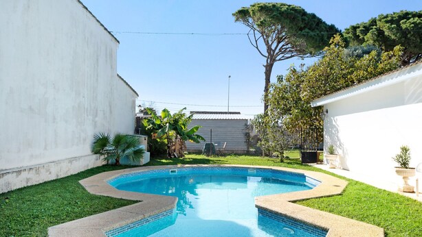 Une piscine dont le bord est recouvert de carreaux, entourée d’une pelouse et d’un mur blanc.