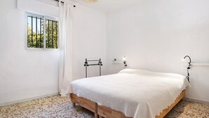 Une chambre à coucher avec un lit, une fenêtre donnant sur un beau paysage, un luminaire suspendu et une étagère fixée au mur.