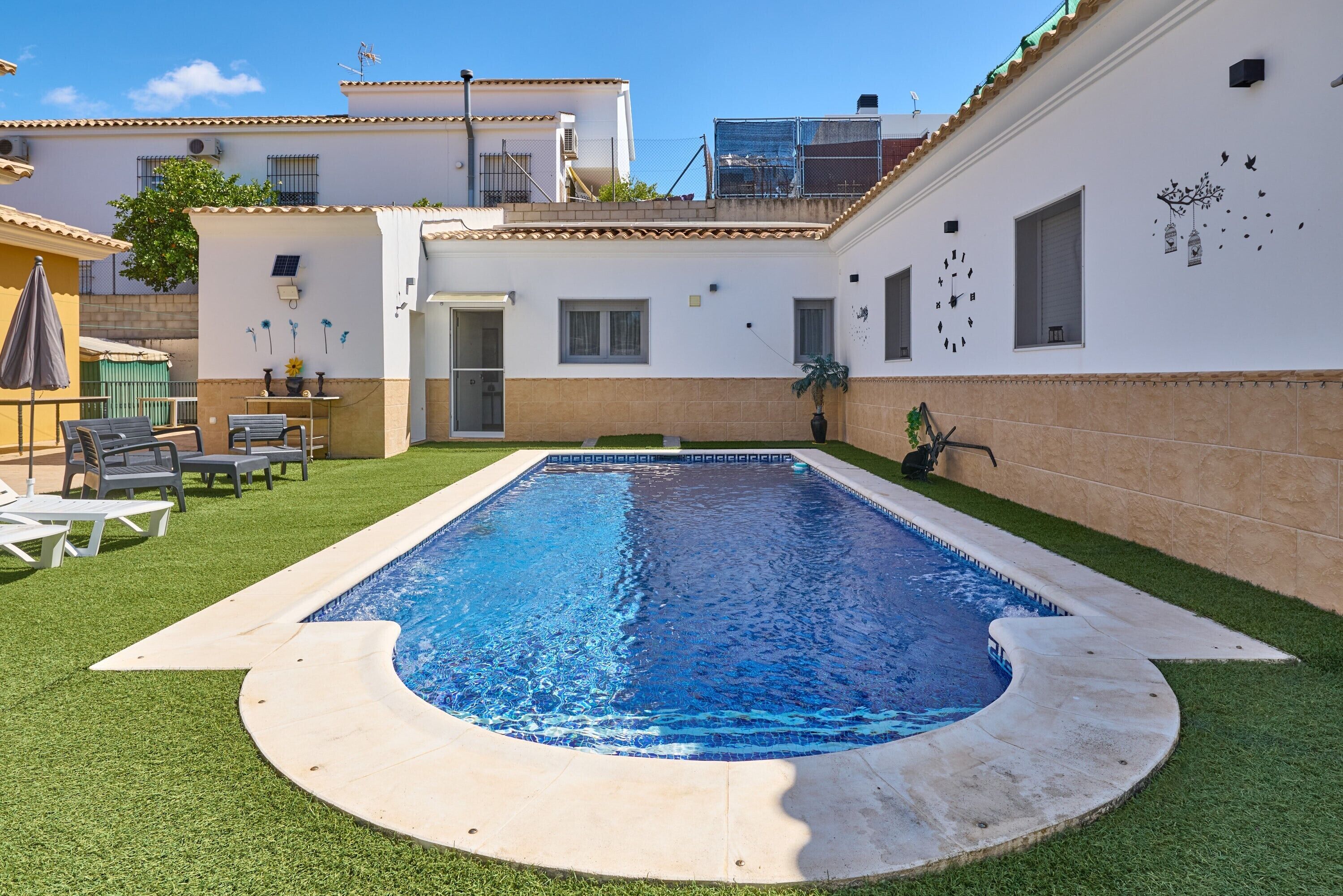 Una piscina con borde de azulejos, rodeada de césped artificial y una solera de hormigón.