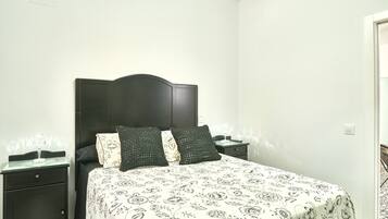 Ein Schlafzimmer mit einem Bett, zwei Nachttischen, einem dunklen Kopfteil und einer zudeckenden Bettwäsche mit Blumenmuster.