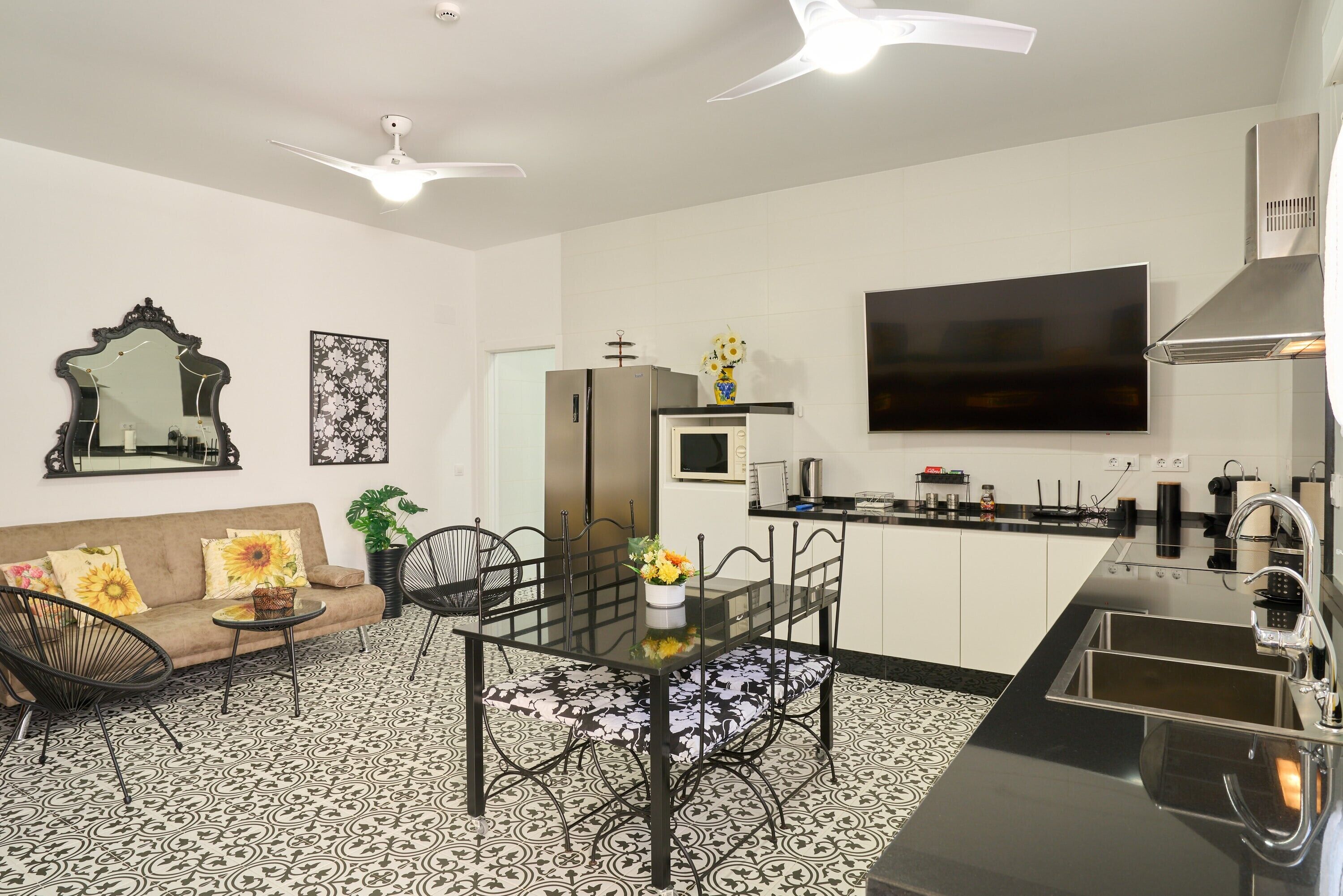 A modern kitchen with a dining area, a flat-screen TV, and a ceiling fan.