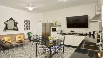 A modern kitchen with a dining area, a flat-screen TV, and a ceiling fan.
