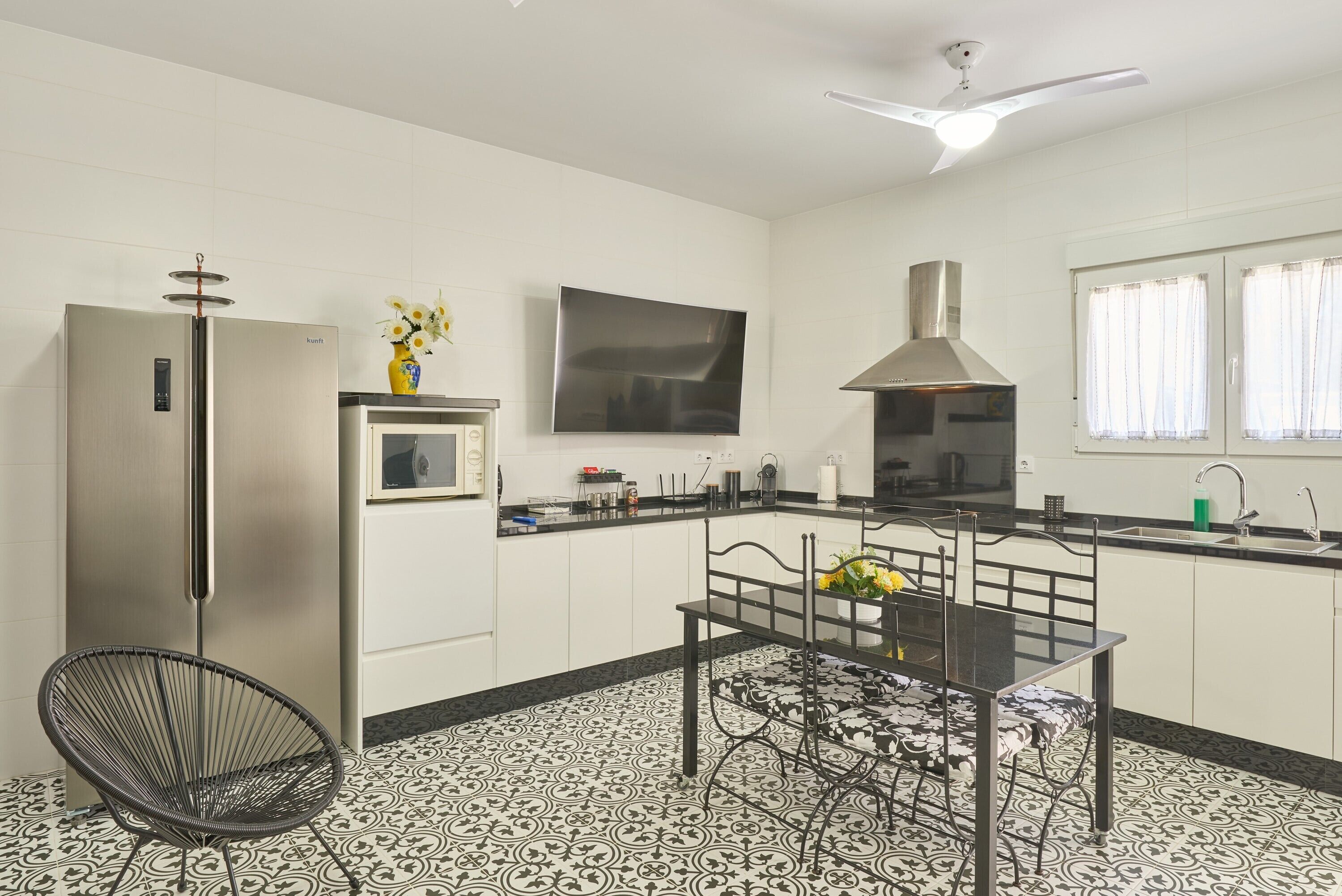 Uma cozinha moderna com forno embutido, mesa de jantar com cadeiras, televisão na parede e ventilador de teto.