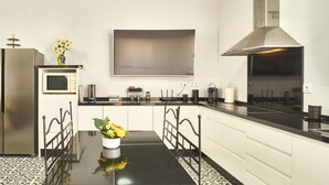 A modern kitchen with a black countertop, white cabinets, a stainless steel refrigerator, a microwave, and a large flat-screen TV mounted on the wall. - Holiday Home 'Marisol' with Shared Pool, Wi-Fi & Air Conditioning (Puente Genil)