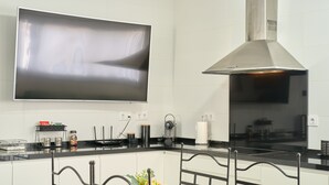 A modern kitchen with a flat-screen TV, stainless steel range hood, and a dining area with a metal chair and a vase of flowers. - Holiday Home 'Marisol' with Shared Pool, Wi-Fi & Air Conditioning (Puente Genil)