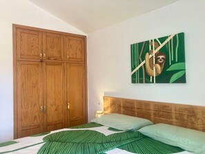 Une chambre avec une grande armoire en bois, un lit avec une literie à rayures vertes et un tableau représentant un paresseux accroché au mur.