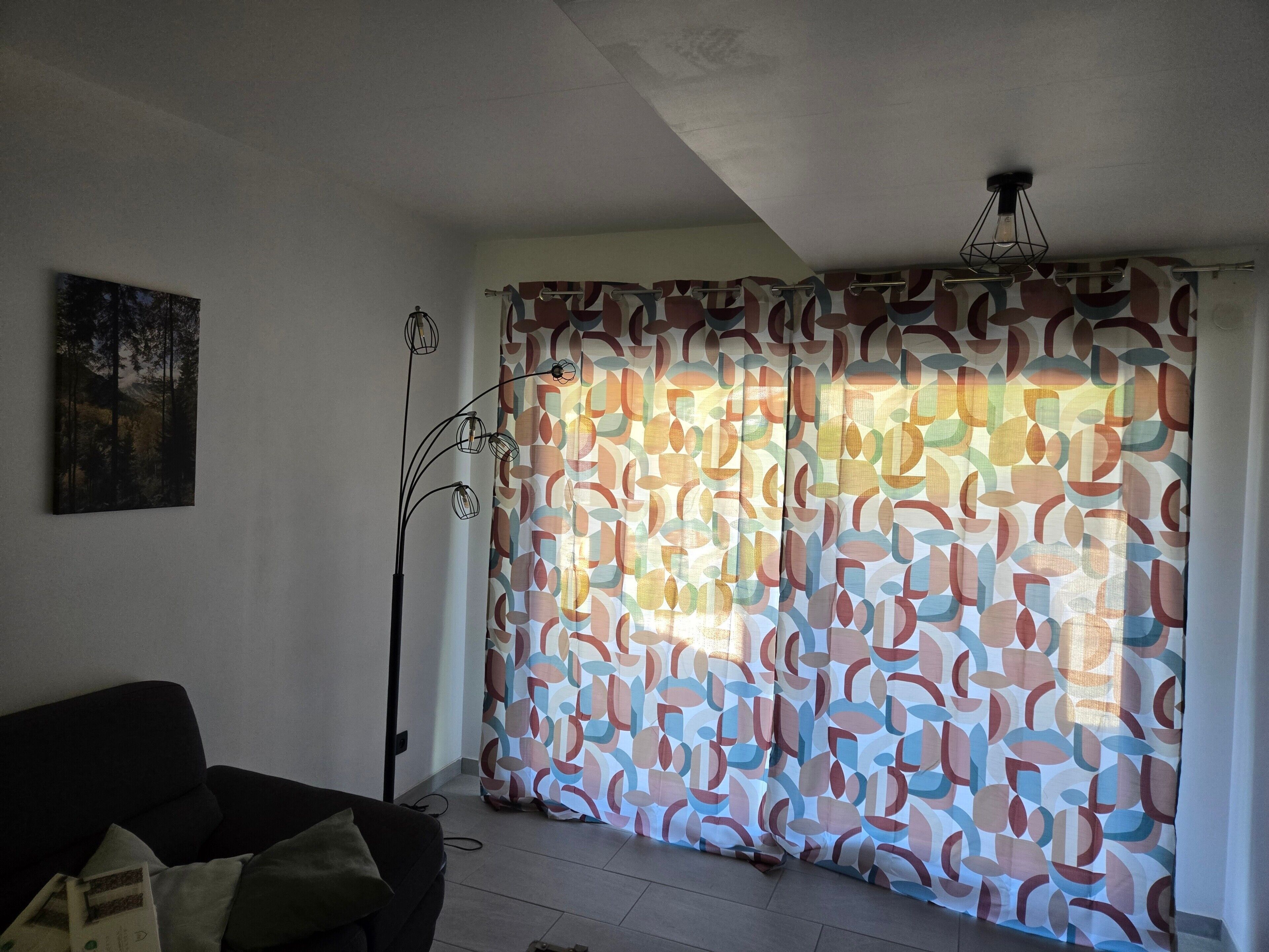 A room with a patterned curtain, a painting on the wall, and a floor lamp.