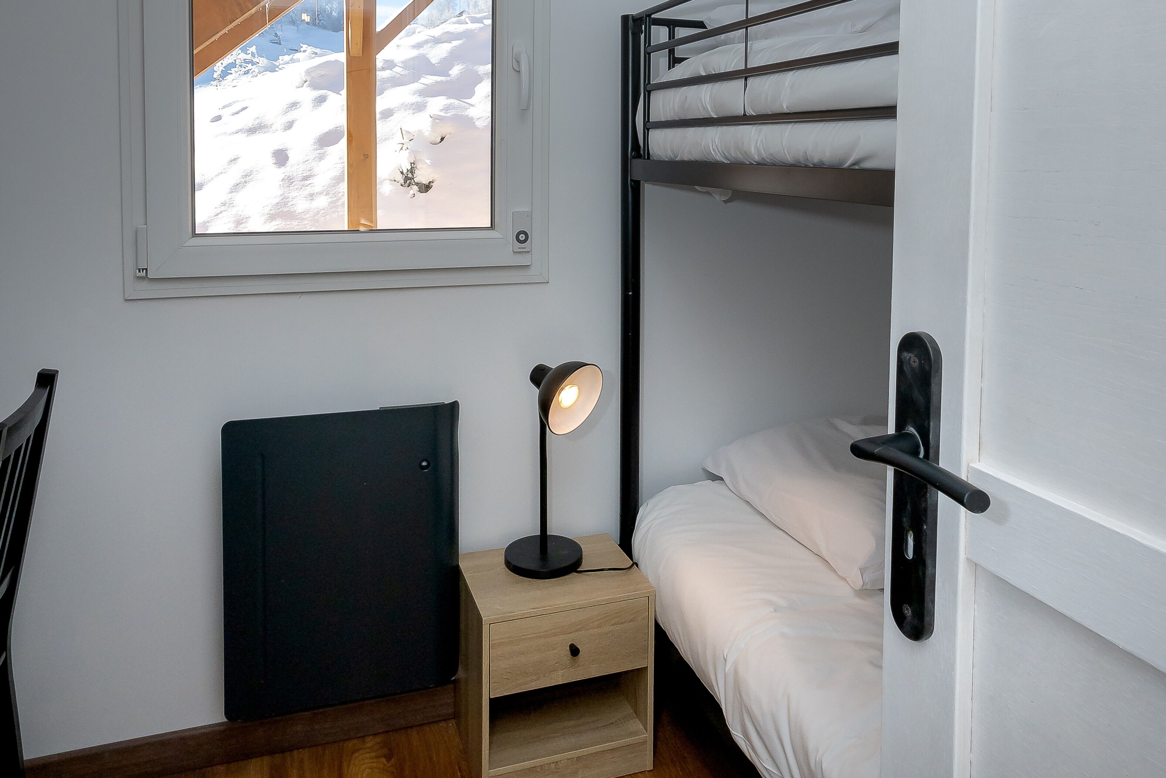 A bunk bed room with a desk, a lamp, and a window with a view of snow.