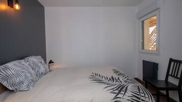 Une chambre à coucher comprenant un lit, une chaise, un bureau, une fenêtre et un luminaire fixé au mur.