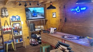 A cozy bar area with wooden walls, a television mounted on the wall, and a neon sign. There are stools and a shelf with various items. - lobo glamp  (Amanalco de Becerra)
