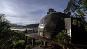 A geodesic dome structure with a metal railing, set against a backdrop of mountains and a body of water. - lobo glamp  (Amanalco de Becerra)