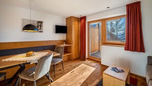 A cozy room with a wooden dining table, chairs, a television, and a large window with curtains.