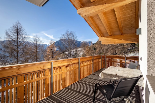 Una terraza de madera con una mesa y sillas, con vistas a un paisaje montañoso.