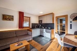 Un espacio habitable compacto con sofá, mesa de centro, mesa de comedor, kitchenette y vistas a través de una puerta de cristal.