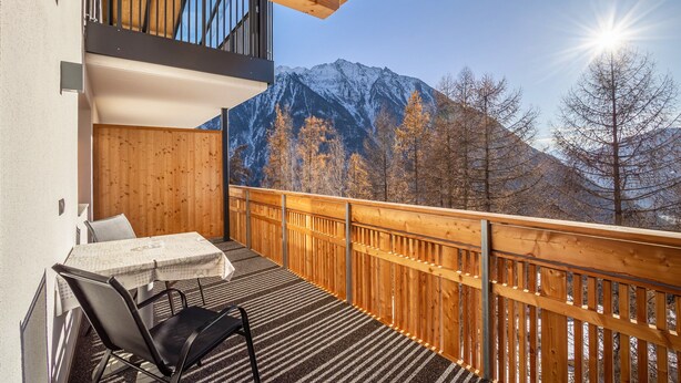 A balcony with a table and chairs, a wooden railing, and a mountain view.