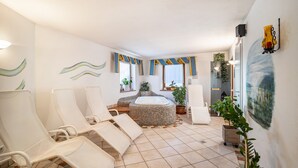 A room with a large bathtub, several lounge chairs, and potted plants.