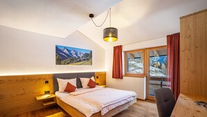 A bedroom with a wooden bed, a desk, a chair, a window with curtains, and a mountain landscape painting on the wall. - Apartment 'Hubertus - Wasserfallspitz' with Mountain View, Private Terrace and Wi-Fi (Sand in Taufers)