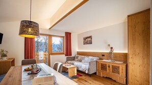 A cozy room with a wooden dining table, a sofa, a small side table, and a cabinet with intricate designs. - Apartment 'Hubertus - Wasserfallspitz' with Mountain View, Private Terrace and Wi-Fi (Sand in Taufers)
