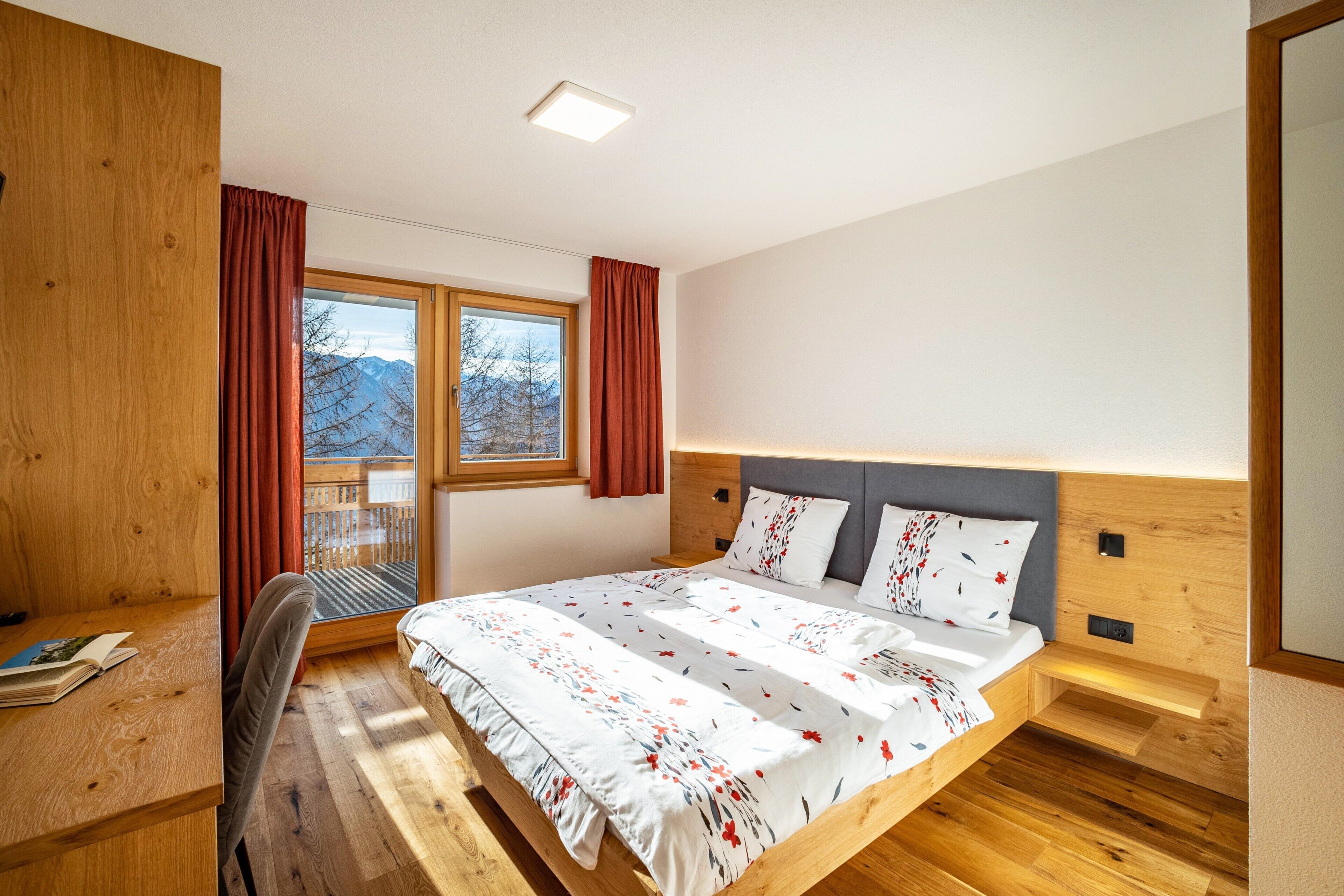 Quarto com cama de madeira, escrivaninha e janela com cortinas.