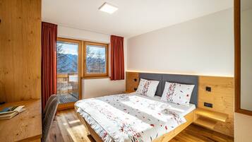 Quarto com cama de madeira, escrivaninha e janela com cortinas.
