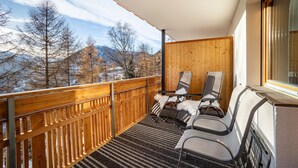 Een balkon met houten leuningen, twee fauteuils en uitzicht op bergen.