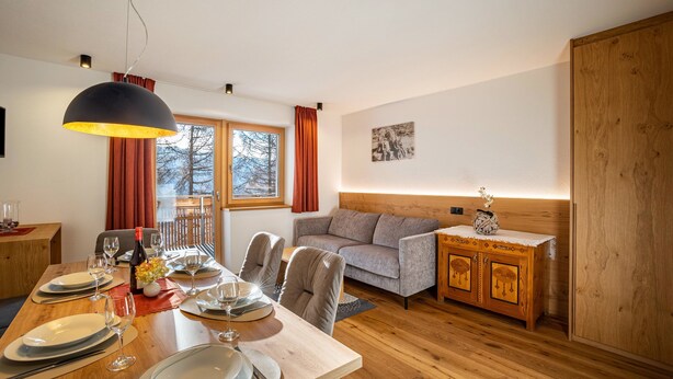Een eetruimte met een houten tafel gedekt voor vier personen, een bank, een kast en een groot raam met gordijnen.
