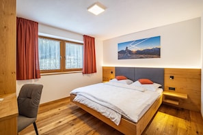 Un dormitorio con una cama de madera, un escritorio, una silla y una ventana con cortinas.