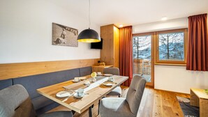 Ein Essbereich mit einem Holztisch, gedeckten Plätzen für vier Personen, grau gepolsterten Stühlen, einer schwarzen Pendelleuchte und einem großen Fenster mit Vorhängen.