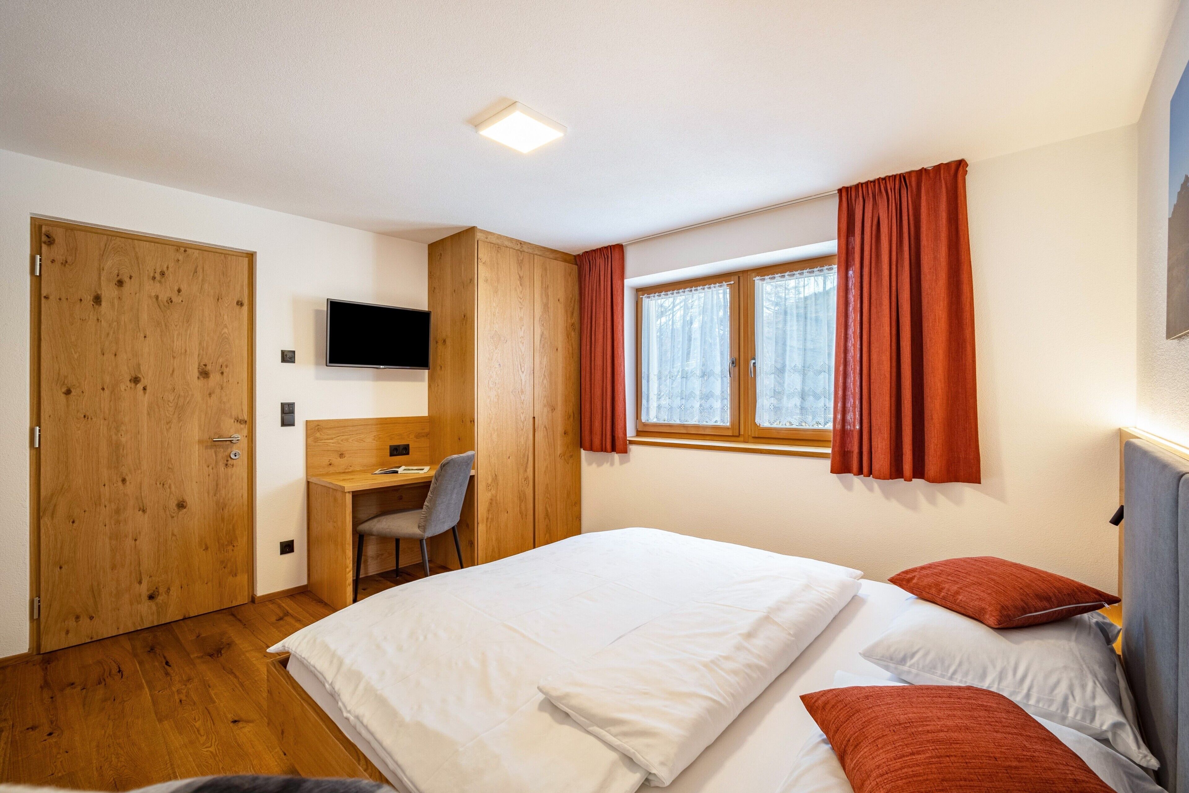 Una camera da letto con un letto, una scrivania, una sedia, una televisione e una finestra con tende.