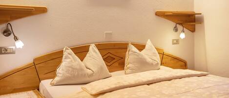 A neatly made bed with pillows and a patterned bedspread, wooden headboard, bedside tables with lamps, and a framed picture on the wall.