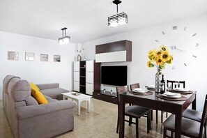 A modern living room with a sofa, dining table, and a flat-screen TV.