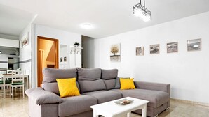 A modern living room with a grey sofa, white coffee table, and yellow cushions. There are framed pictures on the wall and a door leading to another room. - Holiday Apartment "Adosado Conil Centro - Families" with Private Terrace (Conil de la Frontera)