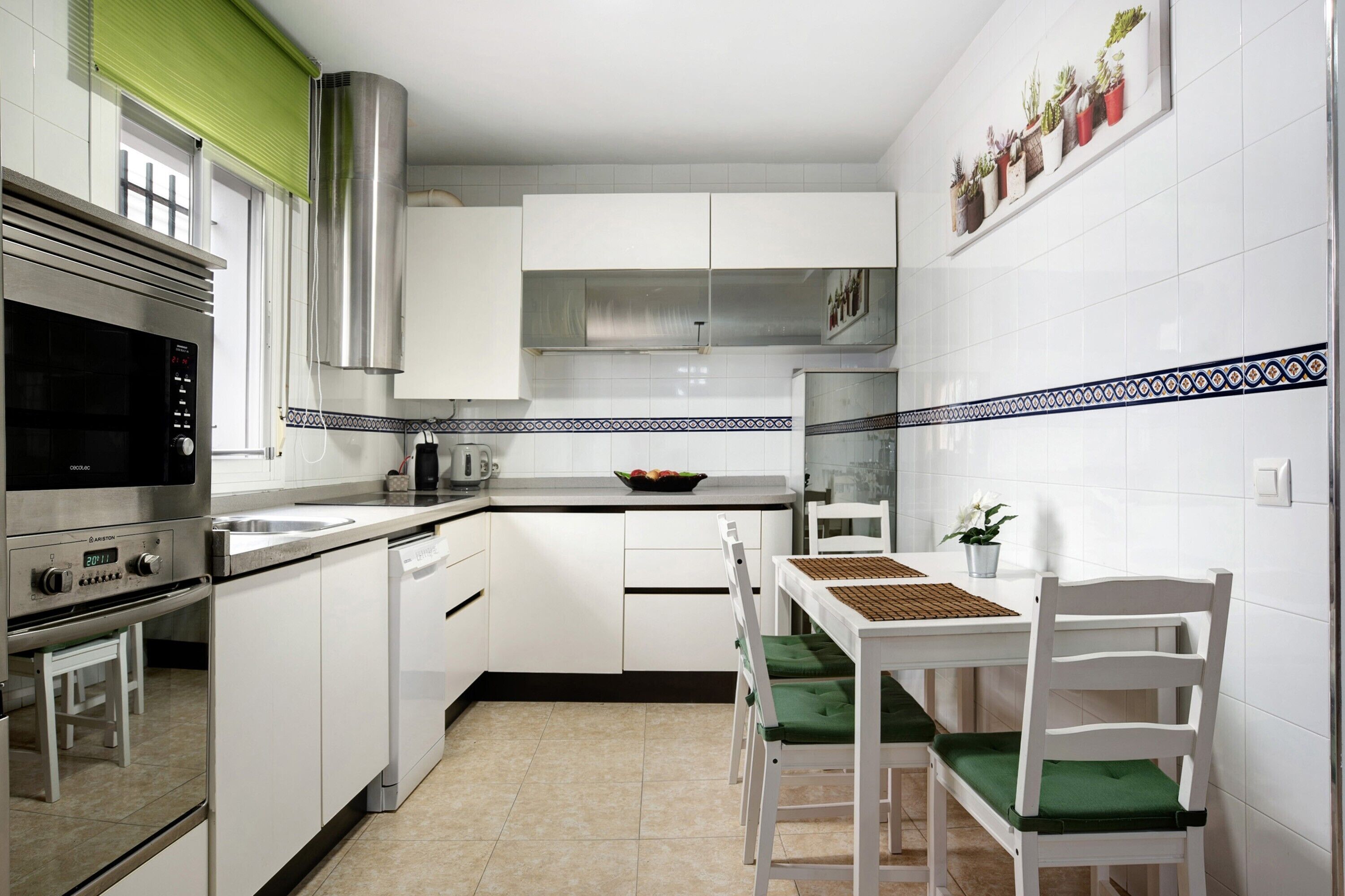 A kitchen with white cabinets, a stainless steel oven, a microwave, and a dining area with a table and chairs.