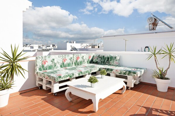 Une terrasse sur le toit, avec un ensemble de meubles de jardin blancs comprenant un canapé et une table basse, ainsi que des plantes en pot.