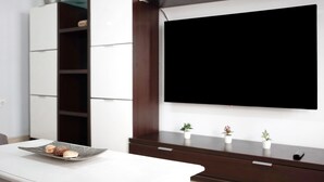 A modern living room with a flat-screen TV mounted on the wall, a white table with decorative shells, and a dark wooden cabinet. - Holiday Apartment "Adosado Conil Centro - Families" with Private Terrace (Conil de la Frontera)