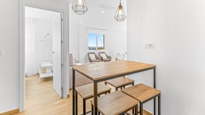 Un espace repas moderne avec une table et des bancs en bois, un éclairage suspendu et une vue sur l’extérieur par une fenêtre.
