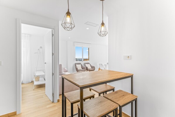 A modern dining area with a wooden table and benches, pendant lighting, and a view of the outdoors through a window.