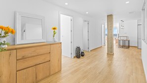 Un intérieur moderne avec un comptoir d’accueil en bois, des murs blancs et un couloir menant à une porte.