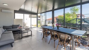 Un salon moderne avec un coin repas, de grandes fenêtres et une vue sur l’extérieur.