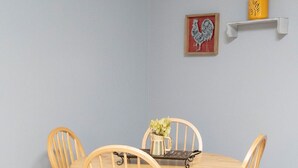 Ein Esstisch mit vier Holzstühlen, einem Blumen-Gießkännchen und einem gerahmten Bild an der Wand.