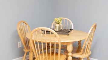 A dining table with four wooden chairs, a pitcher of flowers, and a framed picture on the wall.