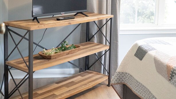 Ein Zimmer mit einem Holzboden-Fernsehschrank, einem Bett und einem Fenster mit Vorhängen.