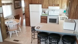 A compact kitchen with wooden cabinets, a white refrigerator, a stove, and a small dining area with a table and chairs.